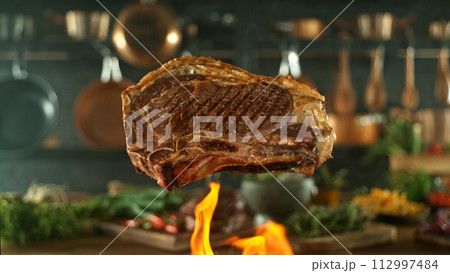 Close-up of tasty beef steak flying above cast-iron grate with fire flames 112997484