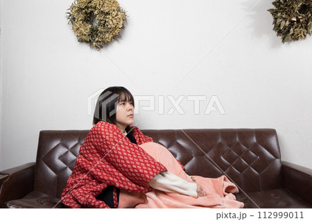 ソファーの上で体育座りをしている女性 ソファーの上で体育座りをしている女性 112999011