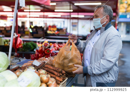 Man in face mask purchasing potatoes in greengrocery Man in face mask purchasing potatoes in greengrocery 112999925