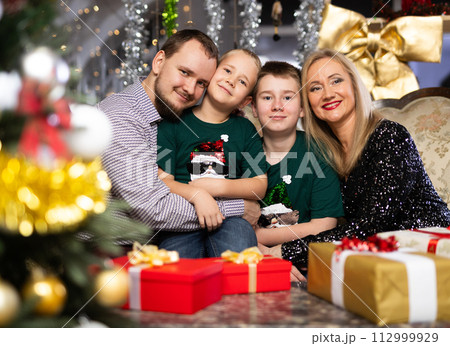 Portrait of happy family with two children celebrating Christmas next to Christmas tree 112999929