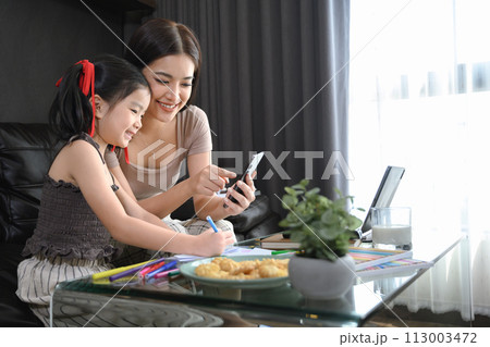 Beautiful Asian mother working at home and taking care of cute little daughter Beautiful Asian mother working at home and taking care of cute little daughter 113003472