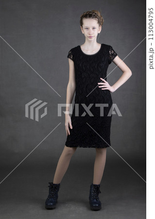 A beautiful thin teenage girl in a black dress and boots is shot on a gray background. A beautiful thin teenage girl in a black dress and boots is shot on a gray background. 113004795