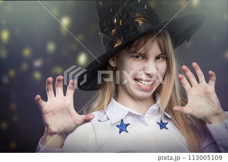 Funny teenage girl wearing Hallow hat makes a frightening gesture on a magical background. Funny teenage girl wearing Hallow hat makes a frightening gesture on a magical background. 113005109