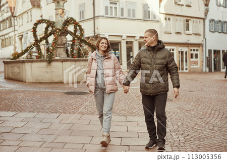 Loving couple of tourists walking around old town. Couple of lovers leisurely stroll in the cool autumn morning on the streets of a BIETIGHEIM-BISSINGEN (Germany). The guy holds his wife. Vacation Loving couple of tourists walking around old town. Couple of lovers leisurely stroll in the cool autumn morning on the streets of a BIETIGHEIM-BISSINGEN (Germany). The guy holds his wife. Vacation 113005356
