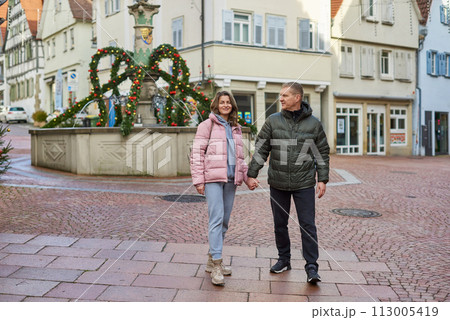 Loving couple of tourists walking around old town. Couple of lovers leisurely stroll in the cool autumn morning on the streets of a BIETIGHEIM-BISSINGEN (Germany). The guy holds his wife. Vacation Loving couple of tourists walking around old town. Couple of lovers leisurely stroll in the cool autumn morning on the streets of a BIETIGHEIM-BISSINGEN (Germany). The guy holds his wife. Vacation 113005419