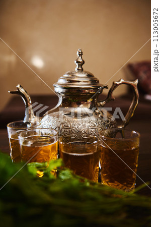 Close-up drinking glasses with fresh Moroccan tea with mint and silver traditional tea pot on wooden table. 113005672