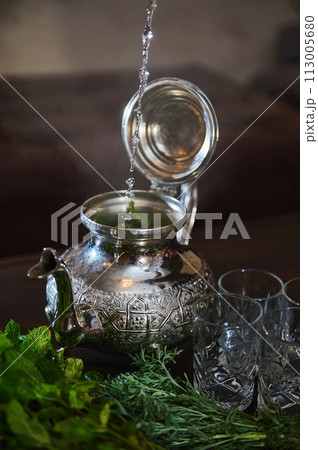 Pouring boiling water into a silver teapot while preparing traditional Moroccan mint tea. Moroccan mint tea Pouring boiling water into a silver teapot while preparing traditional Moroccan mint tea. Moroccan mint tea 113005680
