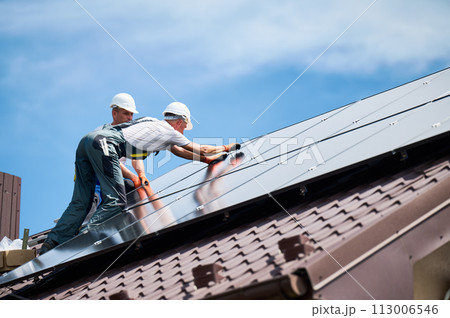 Workers building photovoltaic solar panel system on rooftop of house. Men technicians installing solar module with help of hex key outdoors. Alternative and renewable energy generation concept. Workers building photovoltaic solar panel system on rooftop of house. Men technicians installing solar module with help of hex key outdoors. Alternative and renewable energy generation concept. 113006546