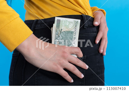 A young woman inserts a bundle of paper banknotes into the back pocket of jeans. A young woman inserts a bundle of paper banknotes into the back pocket of jeans. 113007410