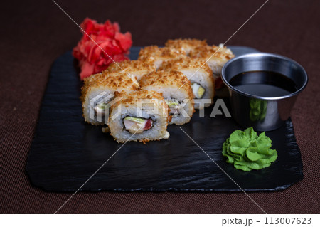 Deep-fried sushi roll with soy sauce and wasabi on a black stone plate 113007623