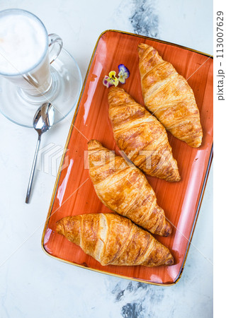 Top view four golden croissants on an orange plate with a cup of coffee on the side Top view four golden croissants on an orange plate with a cup of coffee on the side 113007629