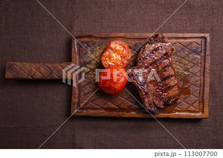 Beef steak with grilled tomatoes on a wooden board Beef steak with grilled tomatoes on a wooden board 113007700
