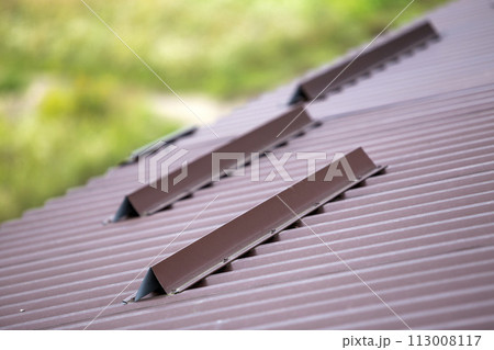 Metal brown shingle tiling house roof surface, rain gutter pipe and snow guards protective fence. 113008117