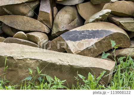 Lit by sun pile of big crackled different sizes and shapes light soft brown stones on green grass. Natural resources, building material, construction and decoration concept. 113008122