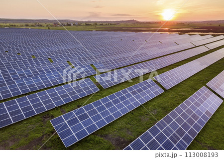 Blue solar photo voltaic panels system producing renewable clean energy on rural landscape and setting sun background. 113008193