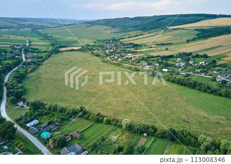 Aerial landscape view of green cultivated agricultural fields with growing crops and distant village houses Aerial landscape view of green cultivated agricultural fields with growing crops and distant village houses 113008346