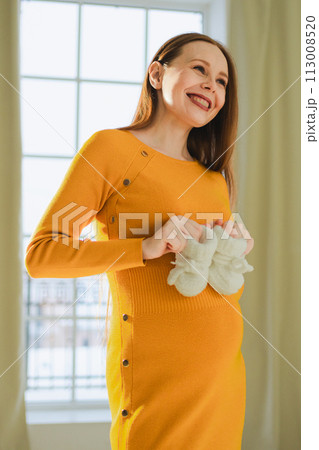 Pregnancy motherhood people expectation future. Pregnant woman with big belly holding newborn baby booties smiling at home. Young mom enjoying pregnancy. Maternity tenderness parenthood new life 113008520
