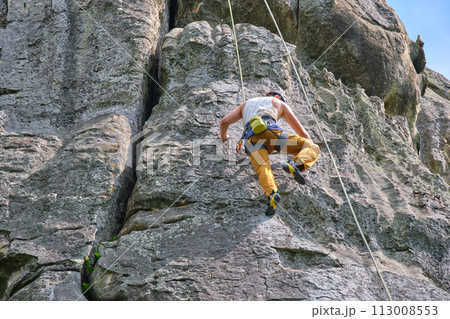 Strong male climber climbing steep wall of rocky mountain. Sportsman overcoming difficult route. Engaging in extreme sports hobby concept. Strong male climber climbing steep wall of rocky mountain. Sportsman overcoming difficult route. Engaging in extreme sports hobby concept. 113008553