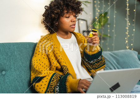 African American woman using laptop shopping online paying with gold credit card. Girl sitting at home buying on Internet enter credit card details. Online shopping ecommerce delivery service 113008819