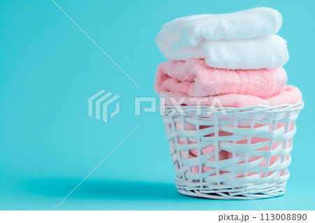 Stack of clean towels in laundry wicker basket on blue background. The towels showcasing their soft and fluffy textures 113008890