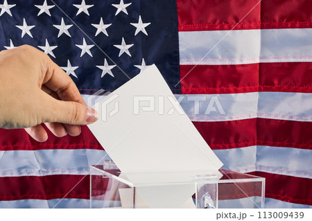 Hand putting his vote into ballot box against national flag of United States 113009439