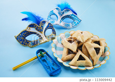 Jewish holiday Purim background with hamantaschen or hamans ears cookies, carnival mask and noisemaker Jewish holiday Purim background with hamantaschen or hamans ears cookies, carnival mask and noisemaker 113009442