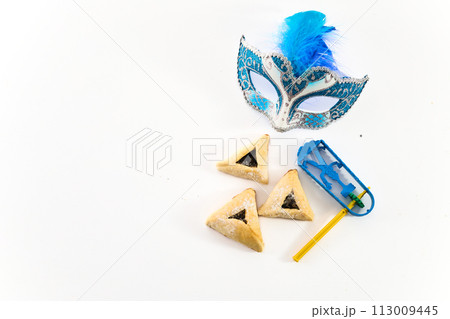 Jewish holiday Purim background with hamantaschen or hamans ears cookies, carnival mask and noisemaker Jewish holiday Purim background with hamantaschen or hamans ears cookies, carnival mask and noisemaker 113009445