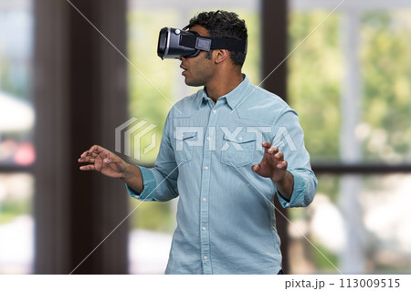 Young scared man wearing virtual reality glasses. Blurred interior background. Young scared man wearing virtual reality glasses. Blurred interior background. 113009515