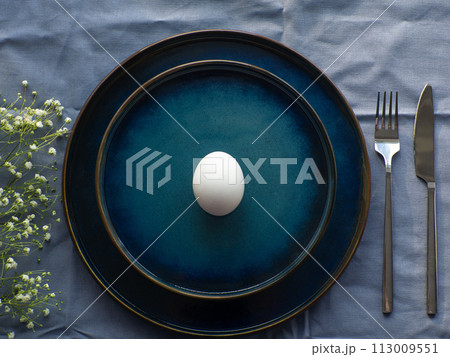 Festive Easter table setting with egg and flowers on blue background Festive Easter table setting with egg and flowers on blue background 113009551