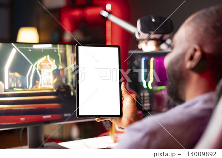 Isolated screen tablet held by gamer competing in online multiplayer videogame at home. Mockup portable device utilized by man playing on gaming PC in neon illuminated apartment Isolated screen tablet held by gamer competing in online multiplayer videogame at home. Mockup portable device utilized by man playing on gaming PC in neon illuminated apartment 113009892