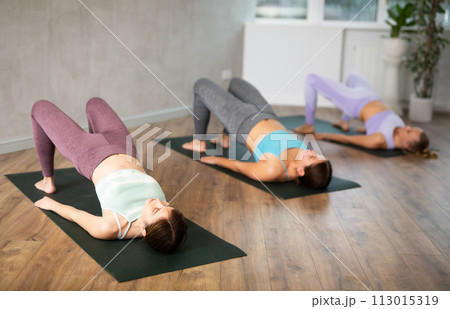 Young female yoga instructor showing others bridge pose in wellness center Young female yoga instructor showing others bridge pose in wellness center 113015319