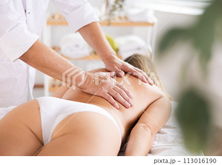 Hands of old masseur conducting back massage for woman client 113016190