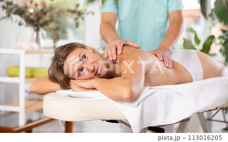 Relaxed middle-aged woman having back massage therapy conducted by skilled masseur 113016205