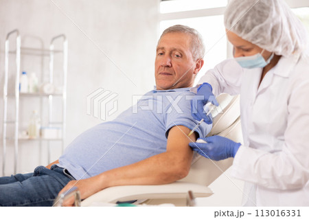 Elderly man getting intramuscular injection in upper arm in medical office 113016331
