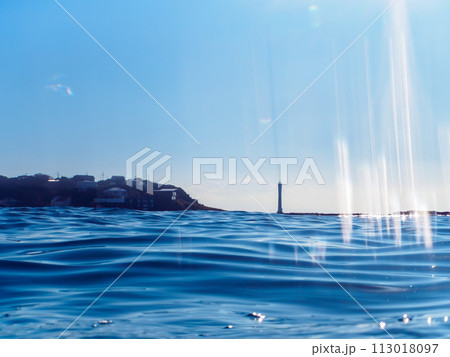 美しい逆光下の白砂のビーチと灯台、海の半水面撮影。 日本国神奈川県三浦市、荒井浜海水浴場にて。 2 美しい逆光下の白砂のビーチと灯台、海の半水面撮影。 日本国神奈川県三浦市、荒井浜海水浴場にて。 2 113018097