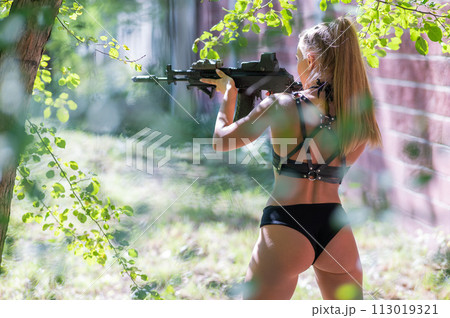 A caucasian woman in a bikini holds a machine gun against a brick wall. A caucasian woman in a bikini holds a machine gun against a brick wall. 113019321