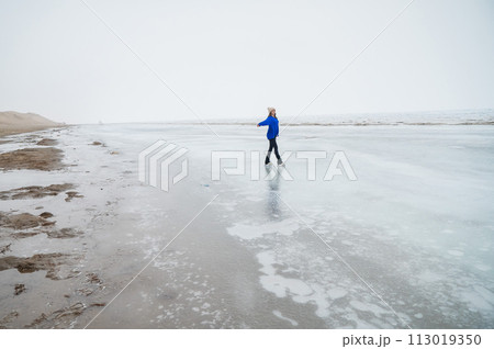 Caucasian woman in a blue sweater is skating on a frozen lake. The figure skater performs the program. Caucasian woman in a blue sweater is skating on a frozen lake. The figure skater performs the program. 113019350
