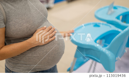 Caucasian pregnant woman chooses a high chair in a children's store. Caucasian pregnant woman chooses a high chair in a children's store. 113019436