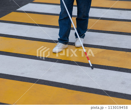 Close-up of the legs of a blind woman crossing the road at a crosswalk with a cane.  113019458