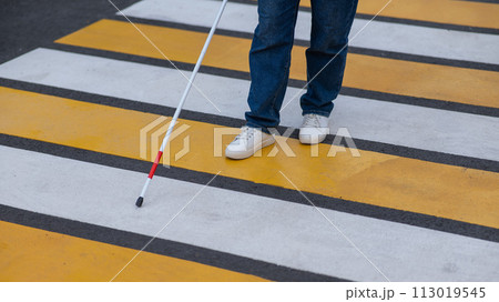 Close-up of the legs of a blind woman crossing the road at a crosswalk with a cane. Close-up of the legs of a blind woman crossing the road at a crosswalk with a cane. 113019545
