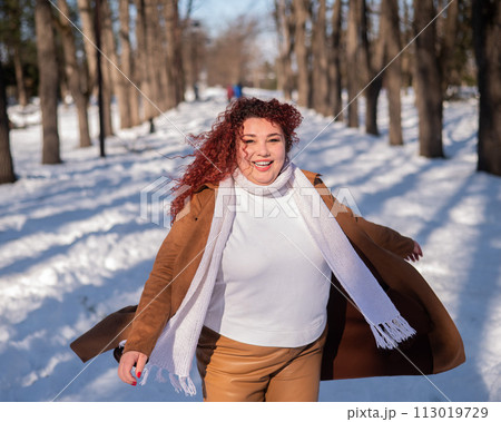 Portrait of an excited red-haired curly fat woman in the park in winter. Portrait of an excited red-haired curly fat woman in the park in winter. 113019729