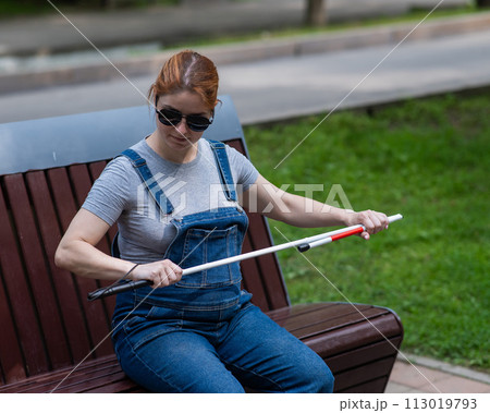 Blind pregnant woman takes out a folding cane while sitting on a bench. Blind pregnant woman takes out a folding cane while sitting on a bench. 113019793