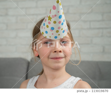 A little Caucasian girl is playing around and wearing a festive hat on her forehead like a unicorn. 113019870