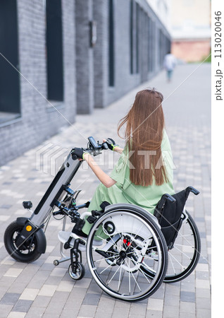 A woman in a wheelchair with an assistive device for manual control. Electric handbike. A woman in a wheelchair with an assistive device for manual control. Electric handbike. 113020046