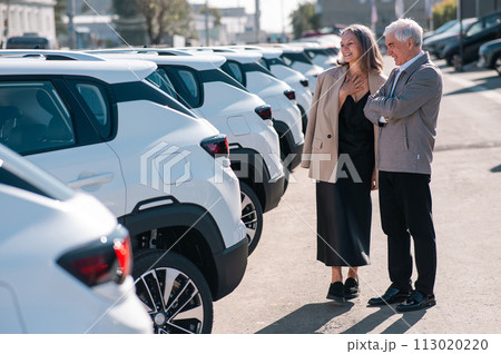 Mature Caucasian couple walks past cars outdoors, choosing a new one.  113020220