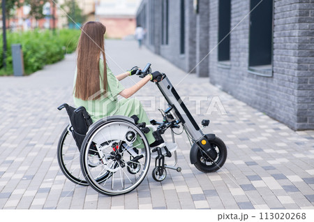 A woman in a wheelchair with an assistive device for manual control. Electric handbike. A woman in a wheelchair with an assistive device for manual control. Electric handbike. 113020268