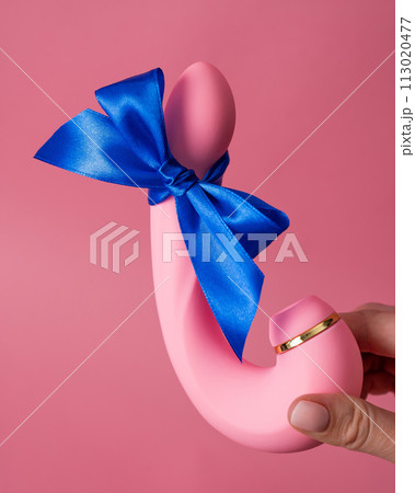 Woman holding curved dildo with blue ribbon on pink background.  113020477