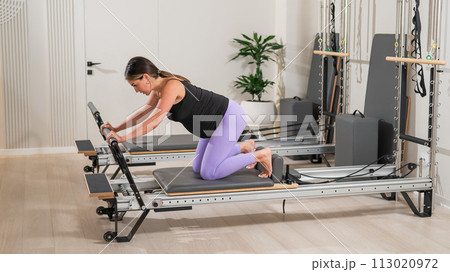 A pregnant woman does a plank on a reformer machine. Perinatal yoga. 113020972