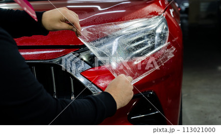 The master applies vinyl film to the headlight of a red car. The master applies vinyl film to the headlight of a red car. 113021000