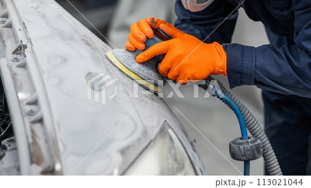 A mechanic sands the putty on a car body with a machine. Repair after an accident. A mechanic sands the putty on a car body with a machine. Repair after an accident. 113021044